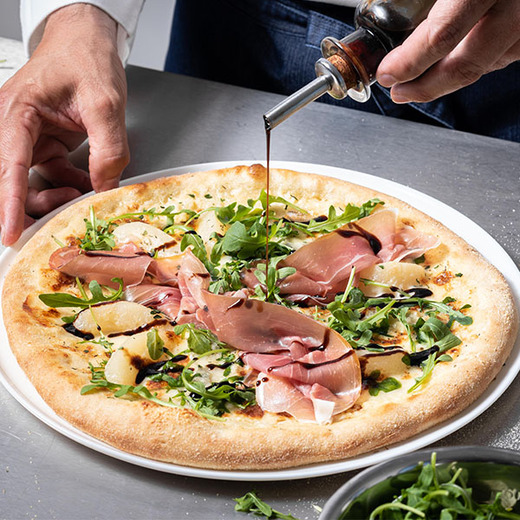 Crème, gorgonzola, poire, fromage italien râpé. Après cuisson : roquette, prosciutto crudo, crème balsamique.