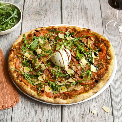 Sauce tomate, pesto vert, fromage italien râpé, tomates. Après cuisson : roquette, mozzarella di bufala, copeaux de fromage italien, crème balsamique Sauce tomate, pesto vert, fromage italien râpé, tomates. Après cuisson : roquette, mozzarella di bufala, copeaux de fromage italien, crème balsamique